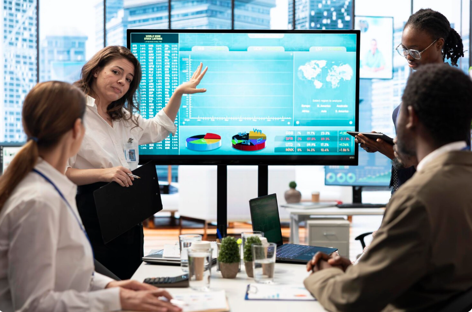 A presenter pointing to a large screen of business performance dashboards during a meeting