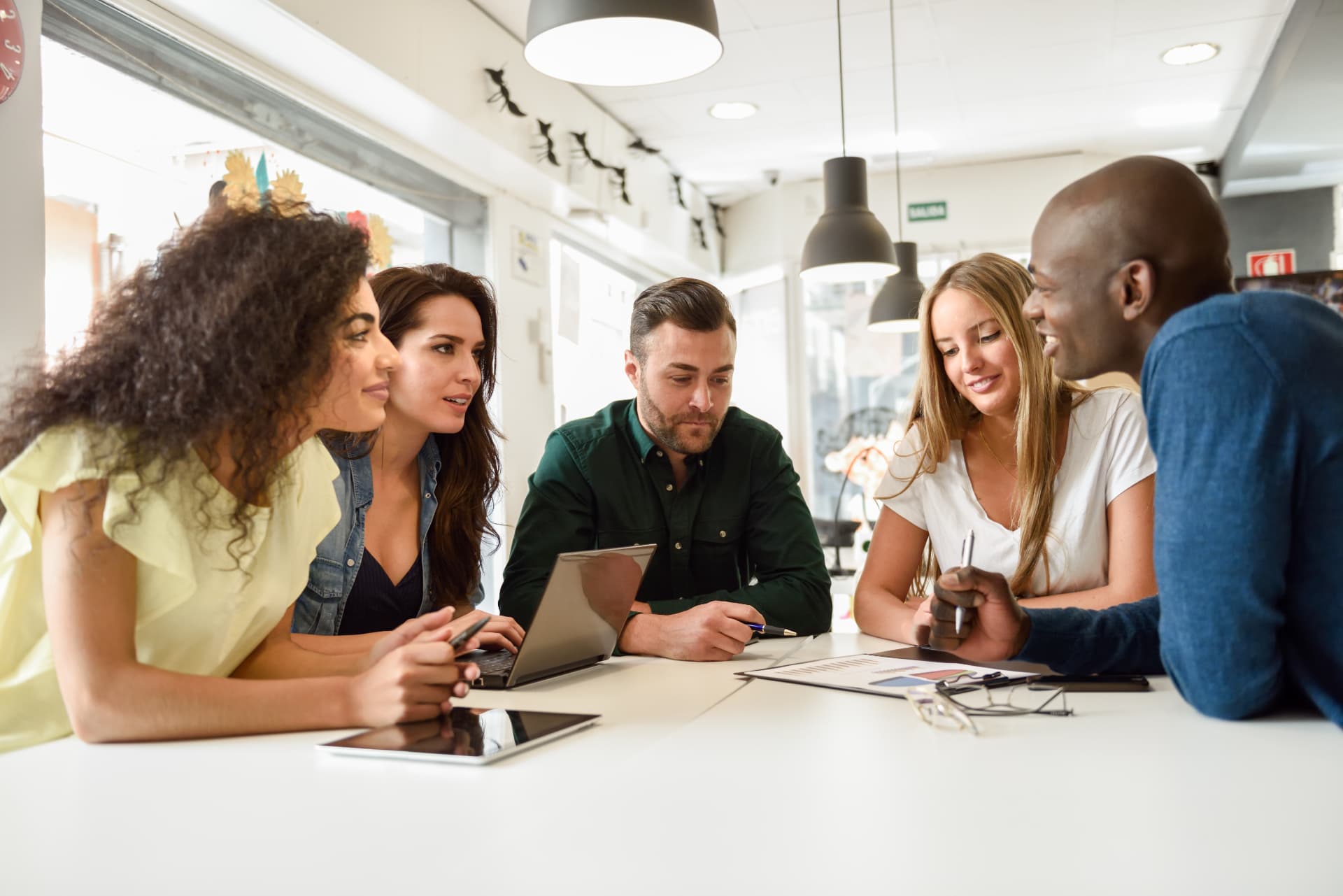 A team gathered around a table discussing work on a laptop and printed reports